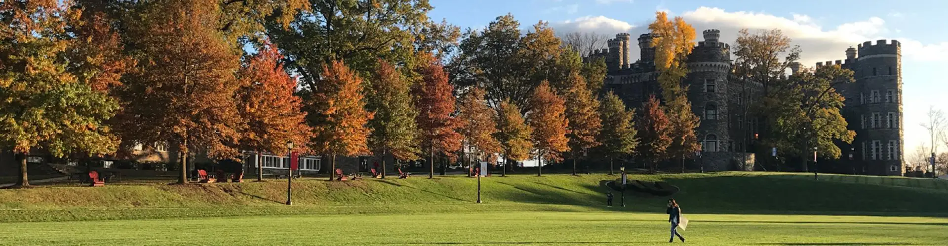 A person walking on Haber Green with the trees and Grey Towers Castle in the background