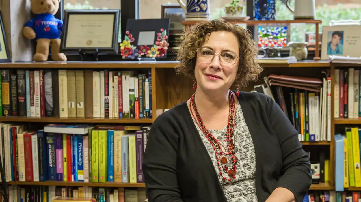 Professor Marianne Miserandino sits in front of an office book case topped with picture frames and decorations.