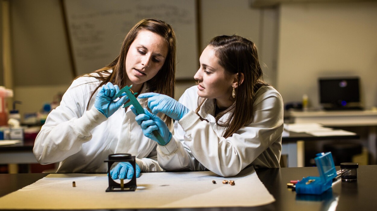 Forensics students examine bullet shells with a caliper.