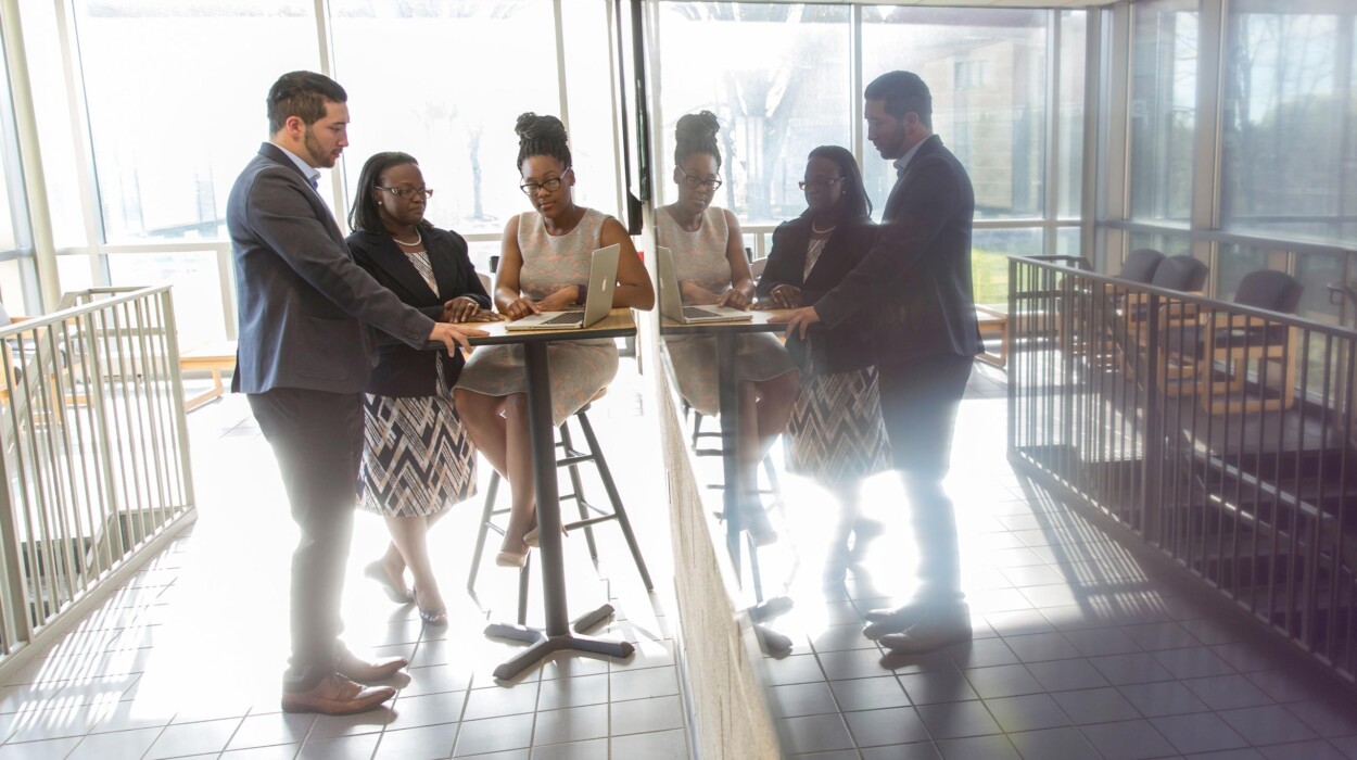 Students gather around a hightop table and look at a laptop.