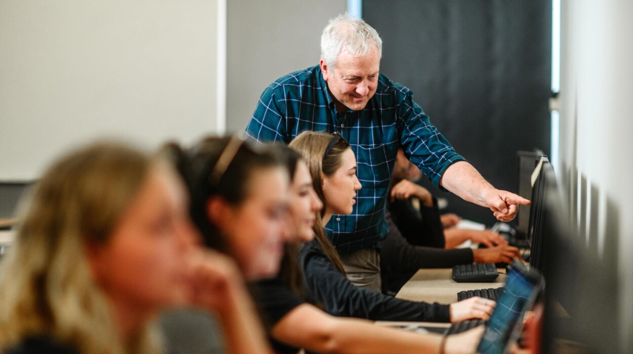 A professor points to a computer screen in a communications lab.