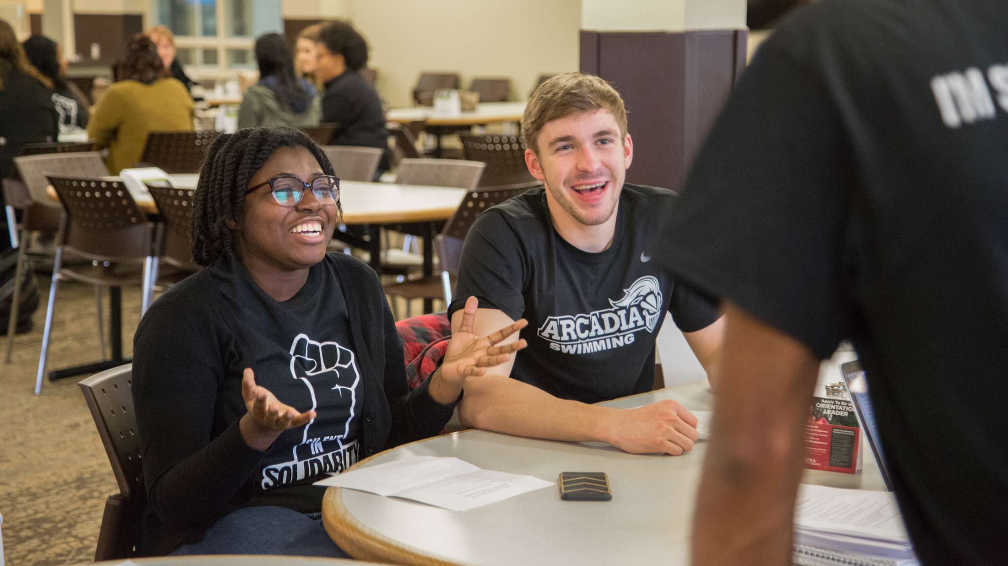 Two students at a table talking to someone