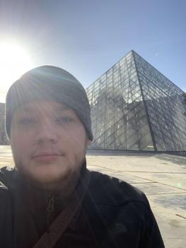 Portrait of a man wearing winter hat standing in front of monument with sun behind him