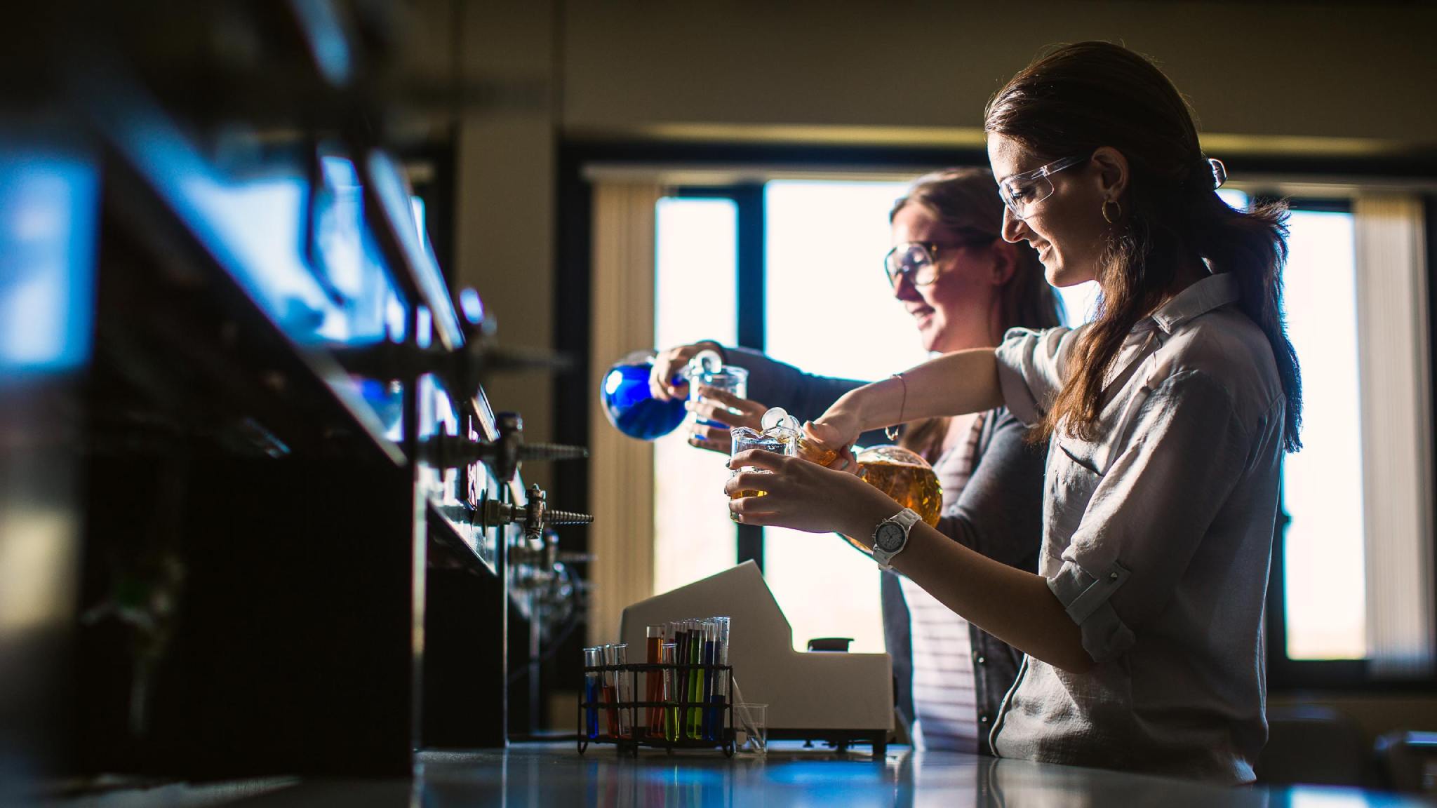 Chemistry students pour liquids in beakers.