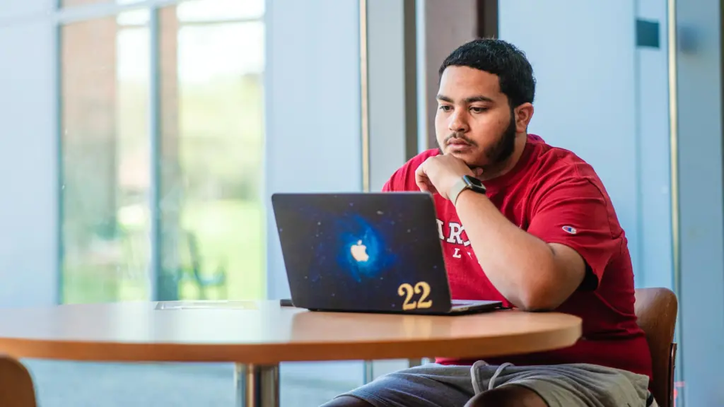 Student uses MacBook laptop at a table indoors.