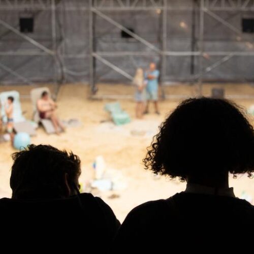 Five people watching an exhibit of people acting like they are on a beach.