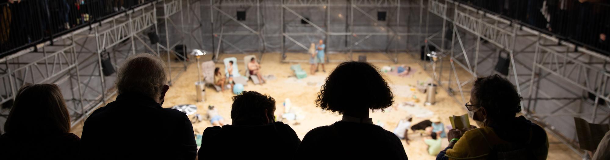 Five people watching an exhibit of people acting like they are on a beach.