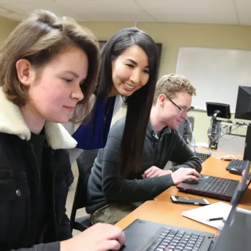 Students interact with a professor in a computer lab.