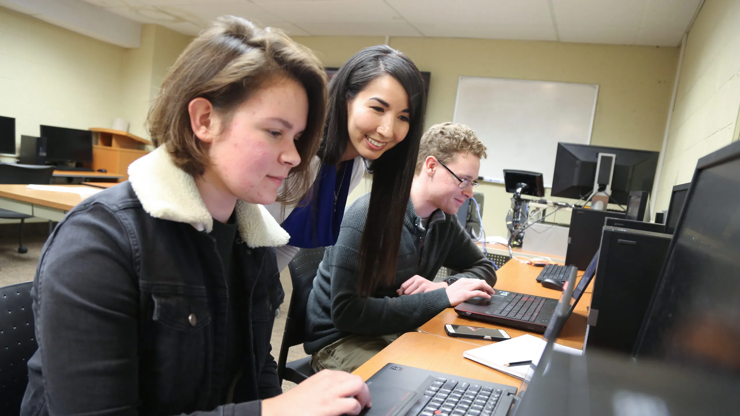 Students interact with a professor in a computer lab.