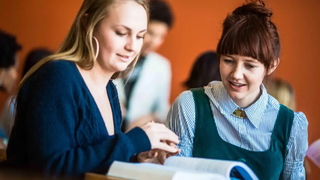 Two students look at a book in a classroom.