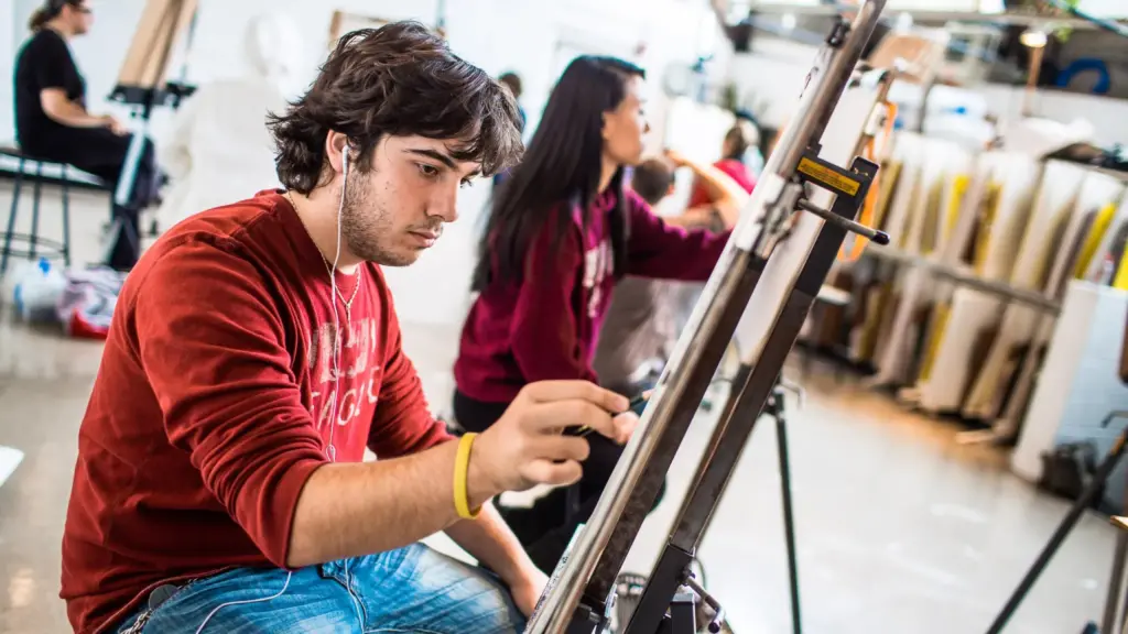 Student draws on a canvas in an art studio while seated.