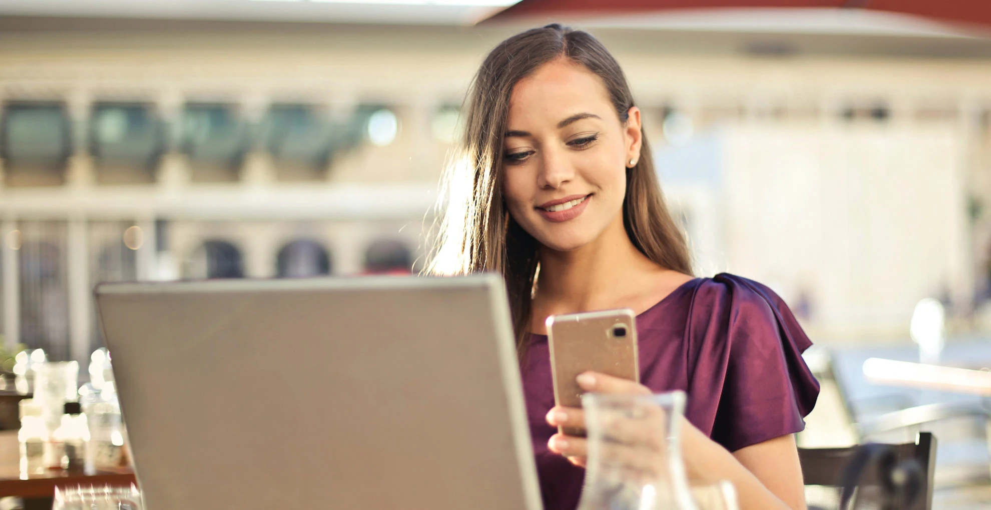 Woman uses laptop and phone at cafe.