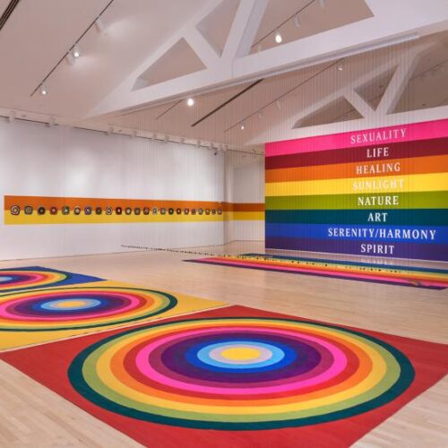 Rainbow circles on the floor of a gym with a rainbow on the wall containing the words "Sexuality, Life, Healing, Sunlight, Nature, Art, Serenity/Harmony, Spirit