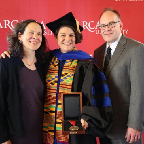 Graduating student standing between two people.
