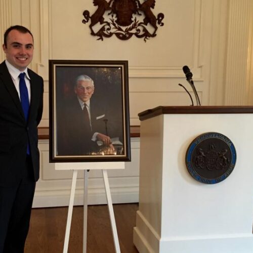 Alex Merker standing next to a painted portrait of James A. Finnegan.