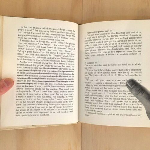 An open book with one real hand on the left side and a photo of a hand on the page on the right side