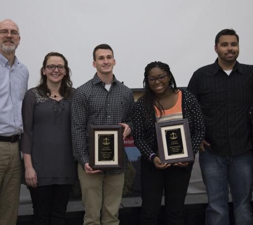 Two among a small group pose while holding plaques