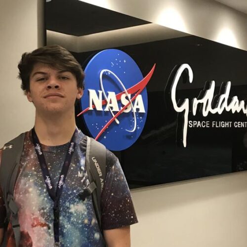 Benjamin Baron stands in from of a sign of the NASA Space Flight Center