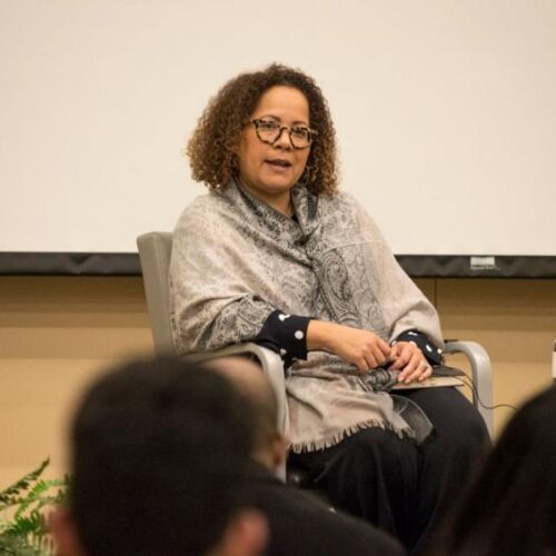 A woman sits in a chair and speaks to an audience