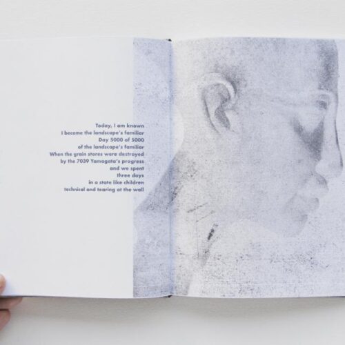 A book is opened to a page that says "Today, I am known / I become the landscape's familiar / Day 5000 of 5000 / of the landscape's familiar"