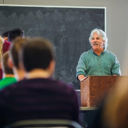 Dr. Morra smiles at a podium in front of his class.