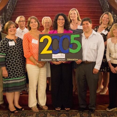 A group of people standing together in front of the stairs inside Grey Towers Castle holding a sign that reads "2005 Doctorate in Special Education"