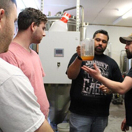 Four men looking at a pitcher in a brew room.