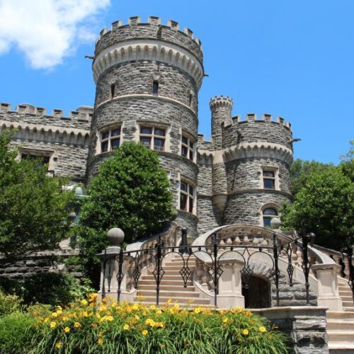 A view of Grey Castle shot in front on the sweeping stairs on a sunny day with yellow daylilies blooming