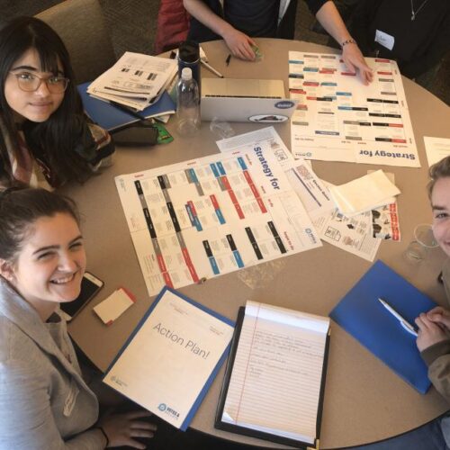 Three students gathered around a table to work on voter turnout Action Plans