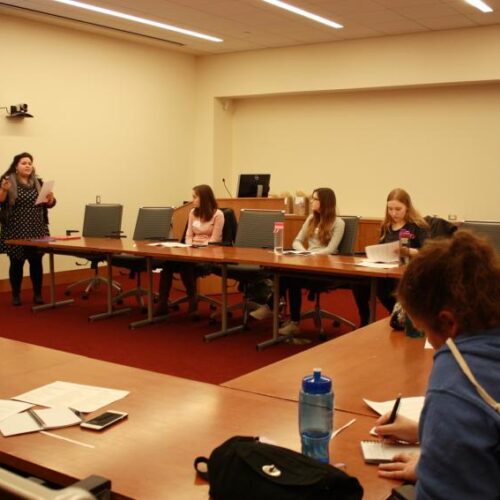 Students sit at tables around a classroom.