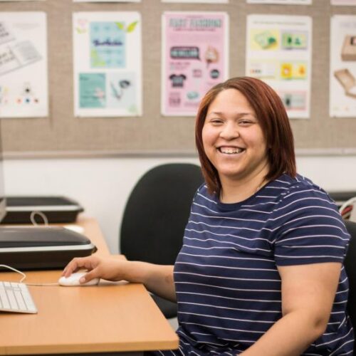 A young woman sitting at a computer, smiling.