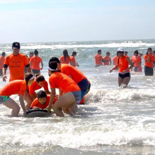 A large group of people wearing orange shirts helping someone on a surfboard
