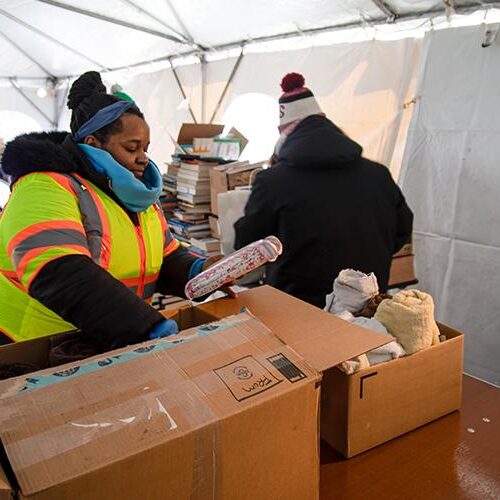 Two people sort boxes in a large tent at a donation center.