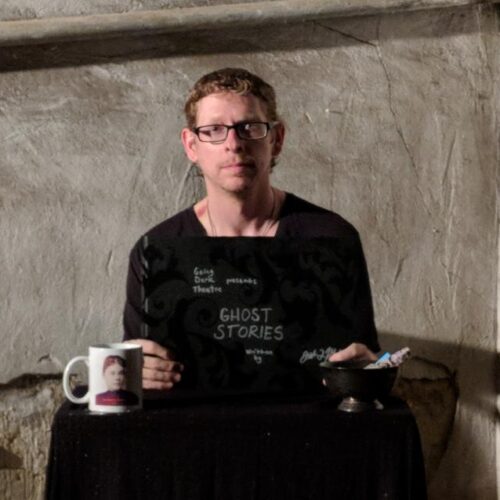 Person sitting at a table with a book titled "Ghost Stories", a coffee cup, and a bowl.