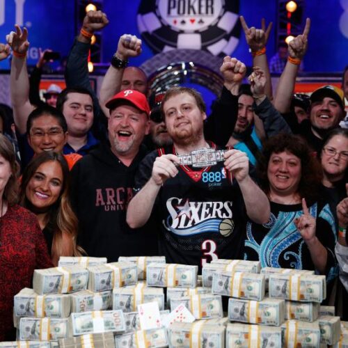 A group of people posing with a person who just won a competition with a pile of cash in front of them.