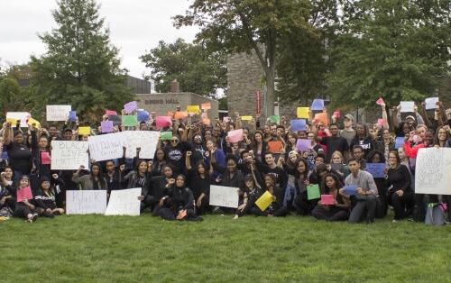 A large group of people dressed mostly in black hold up signs made of poster board and construction paper