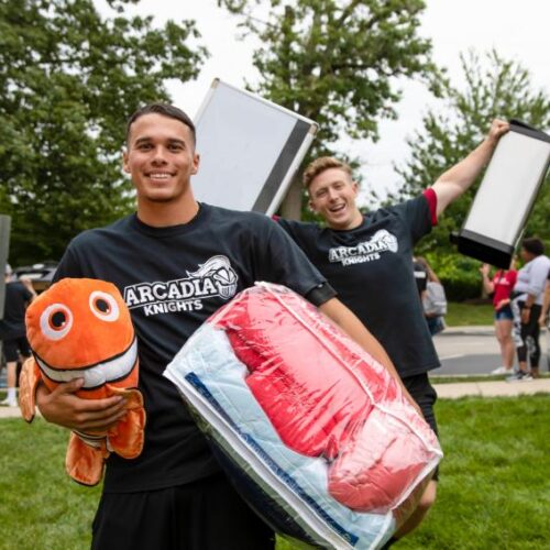 Students carrying pillows and blankets while helping first-year students move into their dorms
