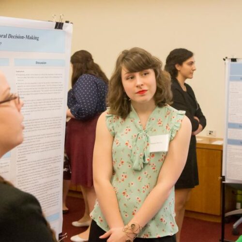 Three women converse in front of a poster that says "Perceived Presence of Moral Decision-Making" Ashley Prue and Morgan McCoy