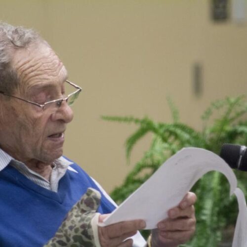 A holocaust survivor reads in front of a microphone