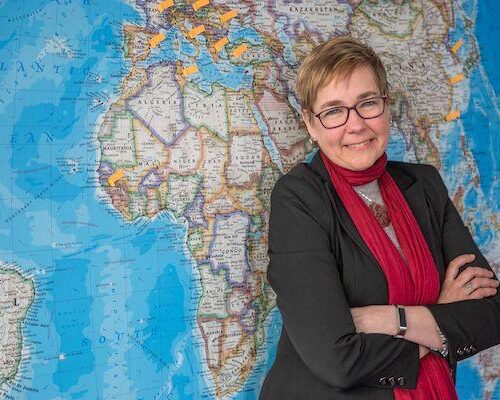 Sandra Crenshaw leans against a large world map.
