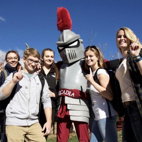 Five students and Archie the Knight mascot all hold up one finger