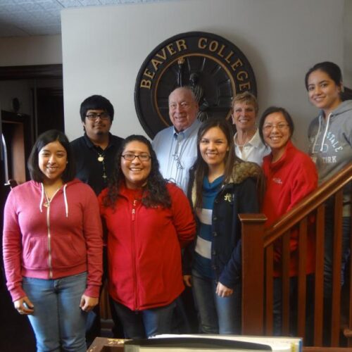 A group poses in Blankley house on the stairs in front of a large Beaver College seal.