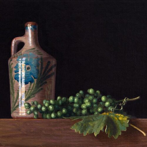 A ceramic floral jug next to a bunch of green grapes or olives