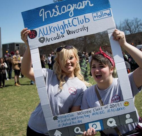 Two people holding a poster that reads "Instagram AU Knight Club" with the center cut out