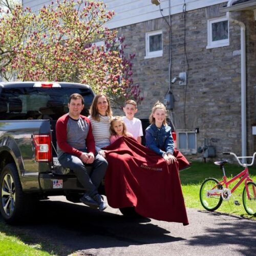 A family sitting in the bed of a truck with a blanket around the youngest child