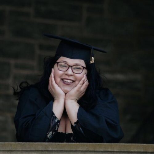 A portrait of a graduate holding their face outside of Grey Towers Castle.