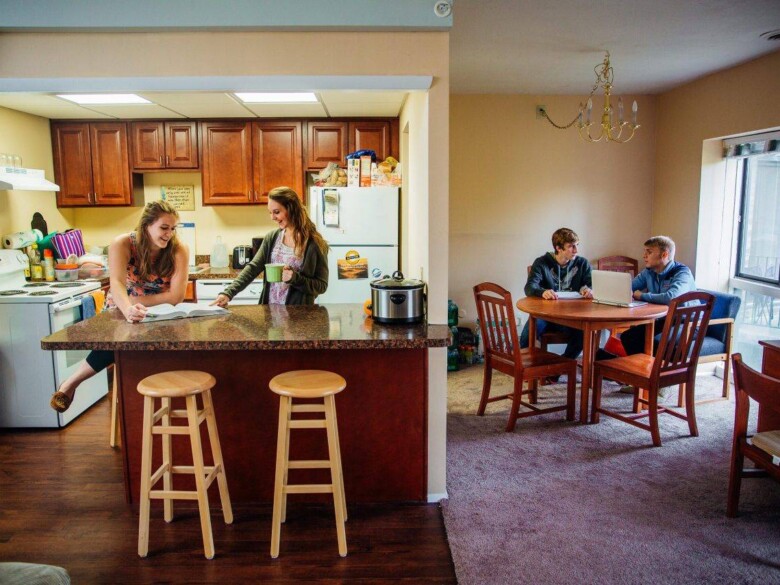 Students congregate around a kitchen island and at a small dining table