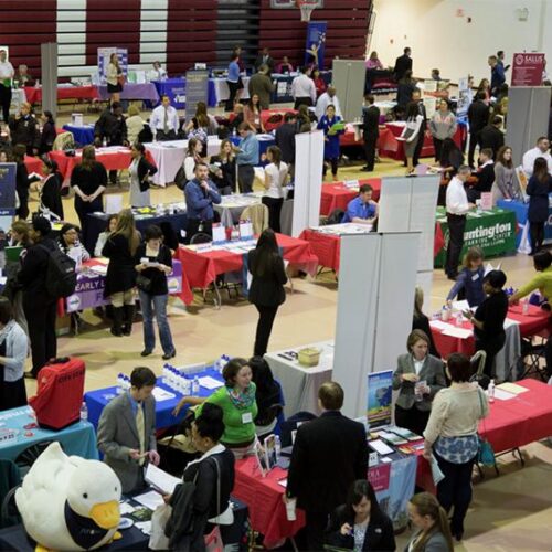 Rows of Career Fair tables and signs with people actively visiting tables in Kuch Center Alumni Gymnasium.