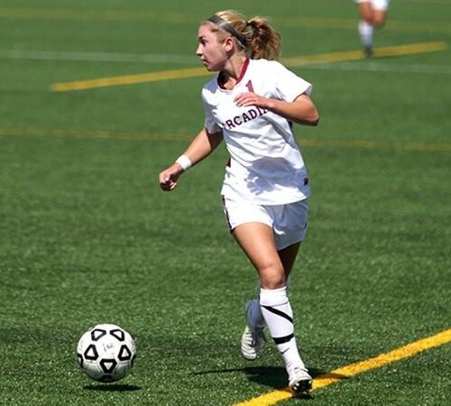 A woman soccer player running next to the ball.