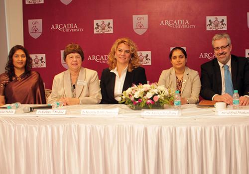 Four women and a man sit at a table topped with a bouquet of flowers and a large Arcadia University banner behind them